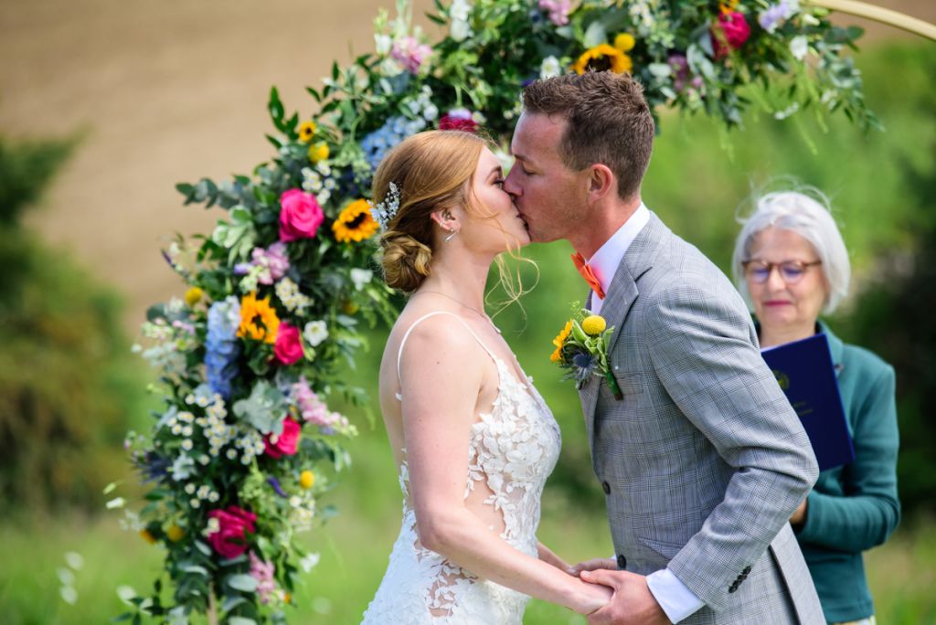 Bride and Groom kissing during meadow wedding ceremony at Monkton Barn.