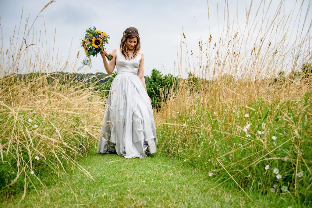 Bride walks through the meadow at Monkton Barn.